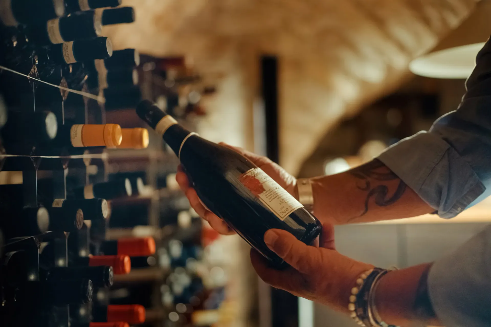A group of five people sitting around a table in a cozy, dimly lit restaurant with stone arched ceiling, enjoying glasses of red wine and smiling at each other