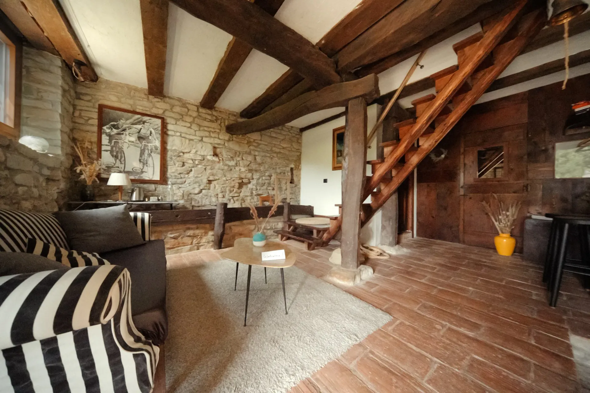 Living room with stone wall, wooden staircase, striped sofa, coffee table, and decorative plants