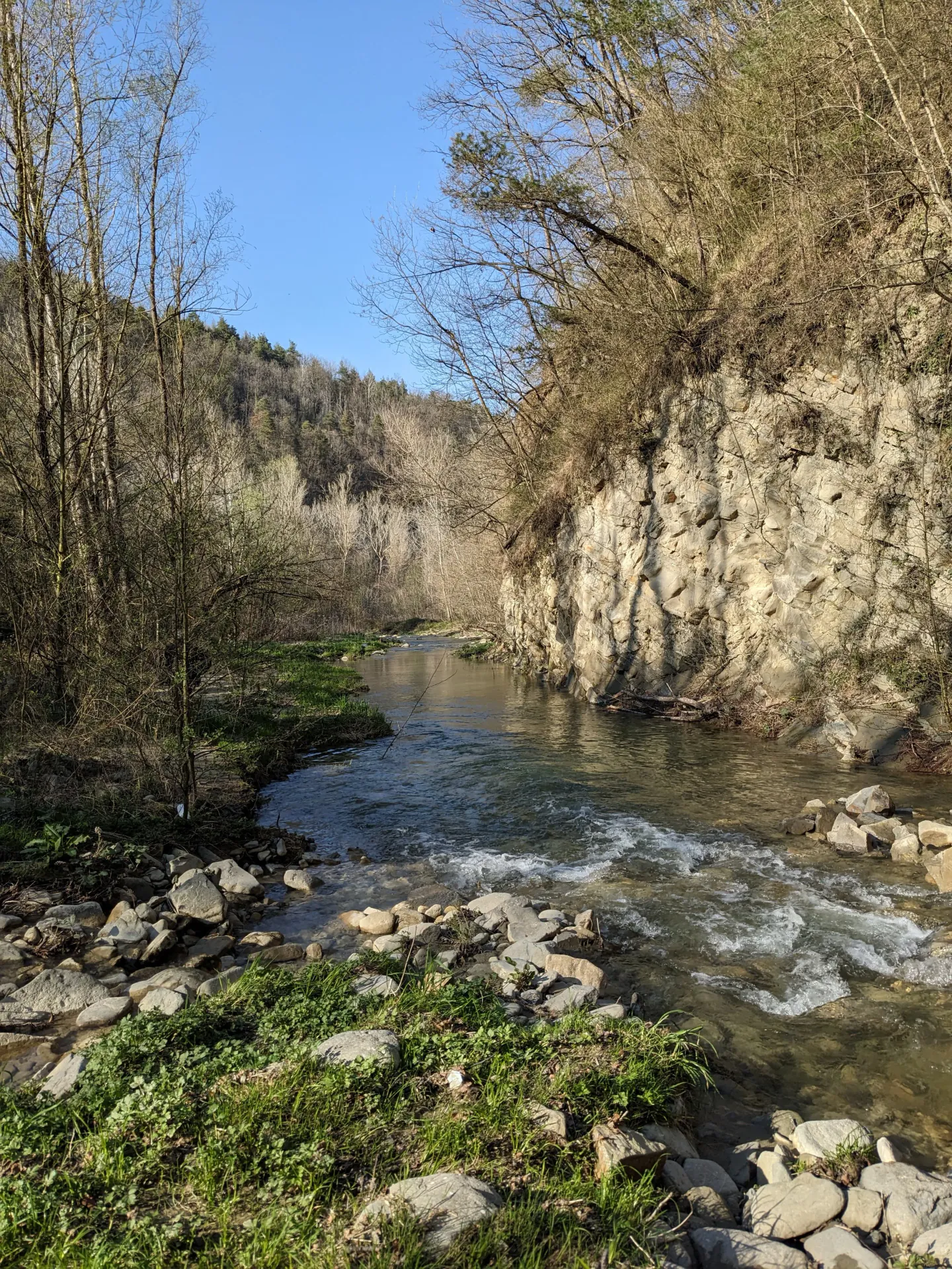 Belbo River (45 minutes of forest-walking away from Doi Fagnàn) flowing through a forested canyon with rocks along the shore and barren trees on the hillside under a clear blue sky. Yes, there is a swimming pool in that part of the river!